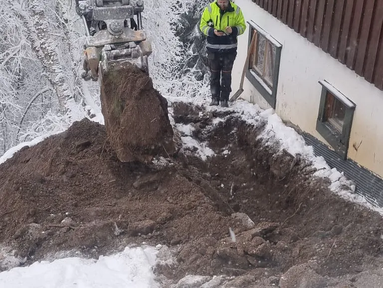 Dränering. Bilden föreställer en grävskopa som gräver ned i jorden runt huset för att skapa rätt djup.